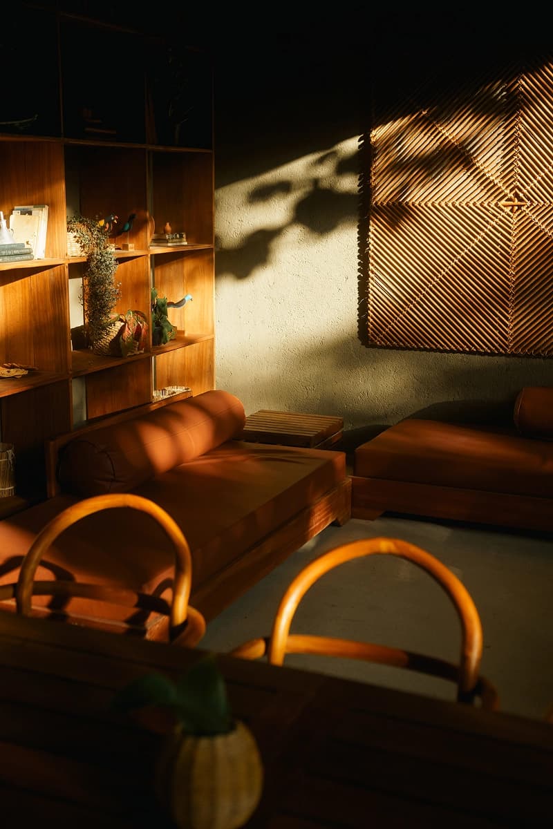 Sala de estar aconchegante com móveis de madeira, almofadas terrosas e luz natural suave